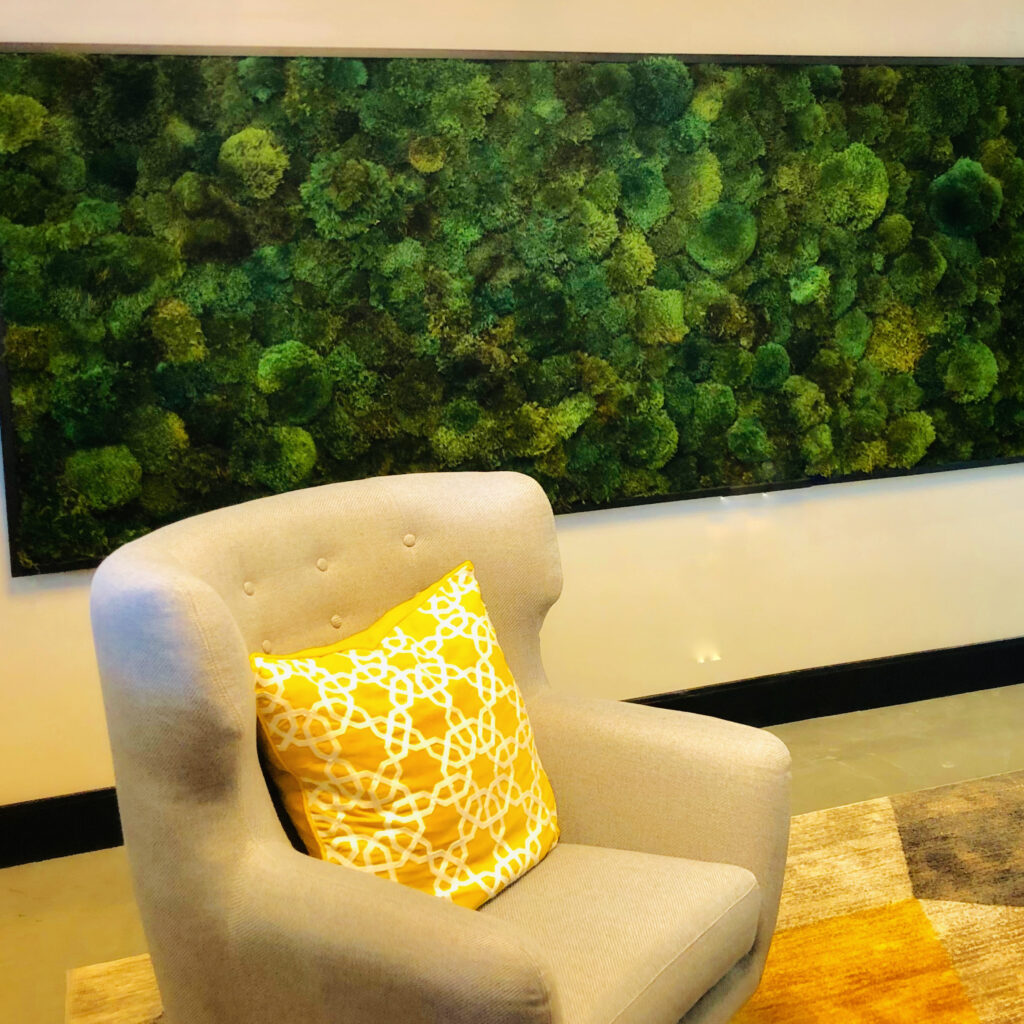 Photo of an 8 foot long lush, green, textured pillow moss frame that encompasses a full wall. This design addresses five of the 14 Patterns of Biophilic Design as put forth by Terrapin Bright Green. 